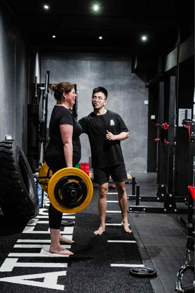 Personal Trainer Sam, correcting a woman's lifting posture during a weight training session at Storm Athletic Club