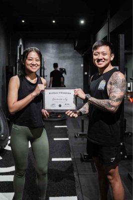 Female gym-goer receiving a Certificate of Wellness from a personal trainer, celebrating achievement at a boutique gym in Singapore.