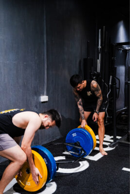 Personal trainer assisting a male client with weightlifting, focusing on proper form and safety at a boutique gym in Singapore.