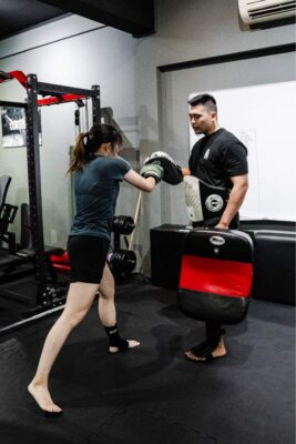 Personal trainer coaching a woman in boxing techniques at a boutique gym in Singapore, enhancing fitness and self-defense skills.