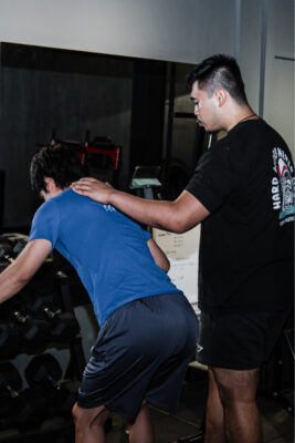 Personal trainer Singapore demostrating safe and effective training technique, correcting a client's posture during a back extension exercise.