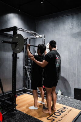 Personal trainers adjusting gym equipment during a training session in Singapore, ensuring optimal setup for effective workouts.