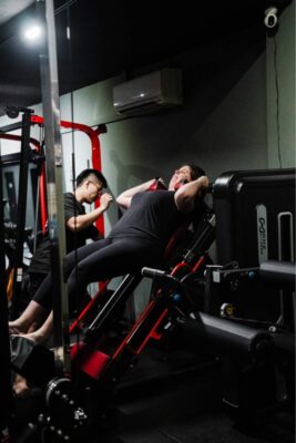 Personal trainer assisting a client on a leg press machine at a boutique gym in Singapore, demonstrating targeted strength training.