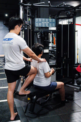 Personal trainer instructing a woman on proper machine use at a boutique gym in Singapore, focusing on safe and effective training.